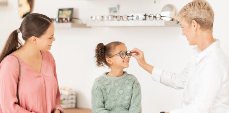 A young girl at the opticians, having her glasses adjusted by the optometrist.