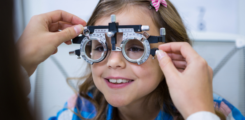 A young girl at the opticians wearing a trial frame during an eye exam.
