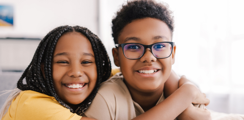 Two children sitting inside smiling, with the boy wearing glasses